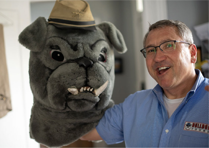 An employee standing next to the Bull Dog mascot